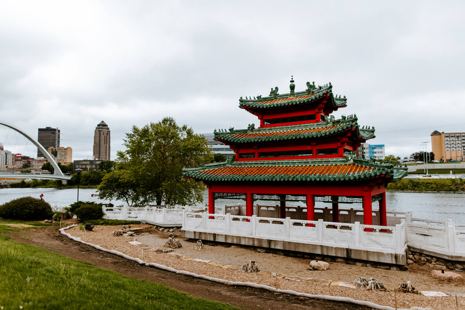 Red Asian Pavilion with a river and city skyline behind it.