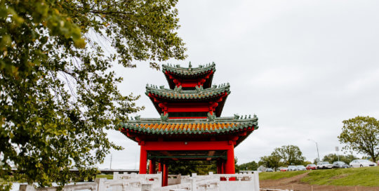 A white bridge leading to a red Asian Pavilion.