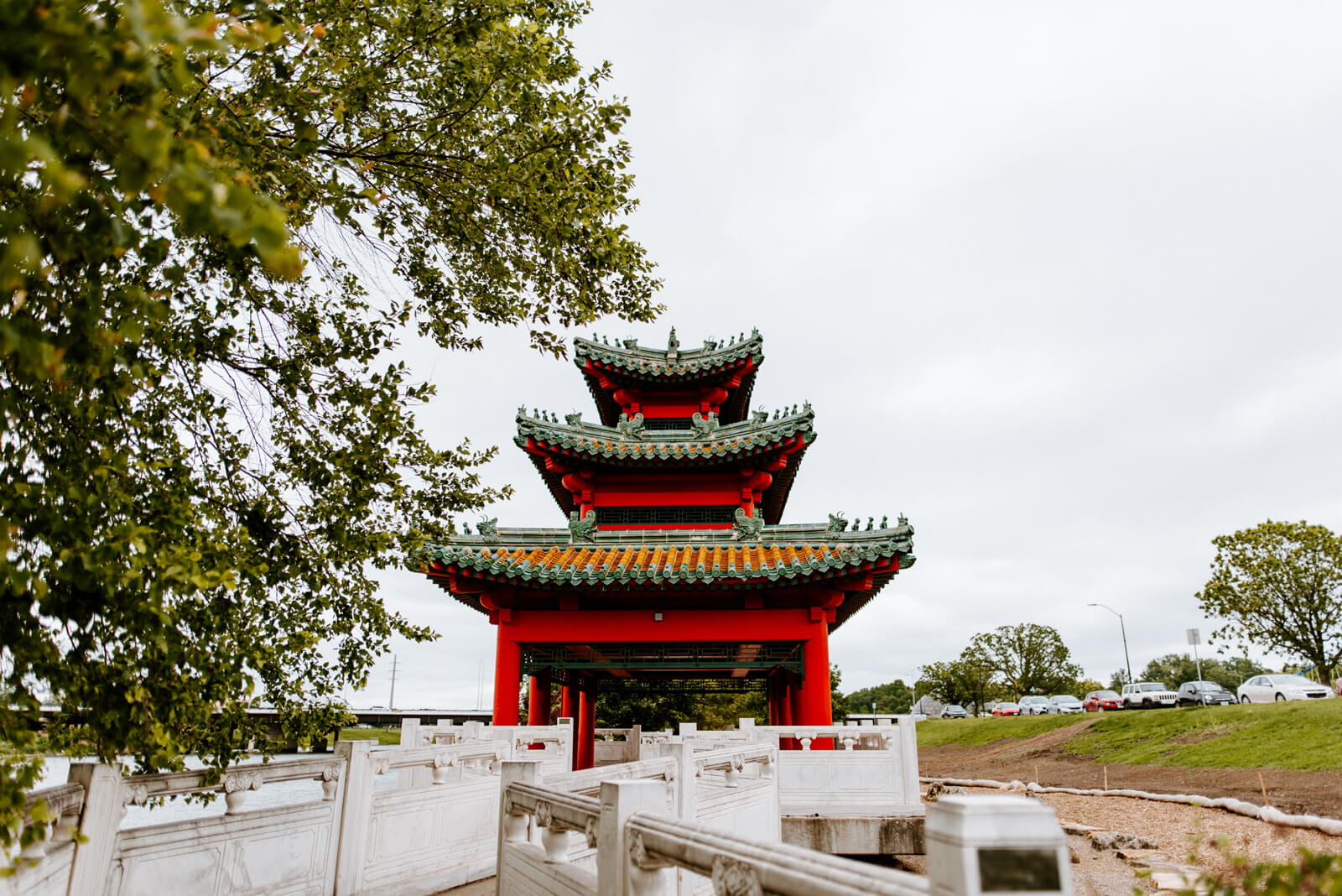 A white bridge leading to a red Asian Pavilion.