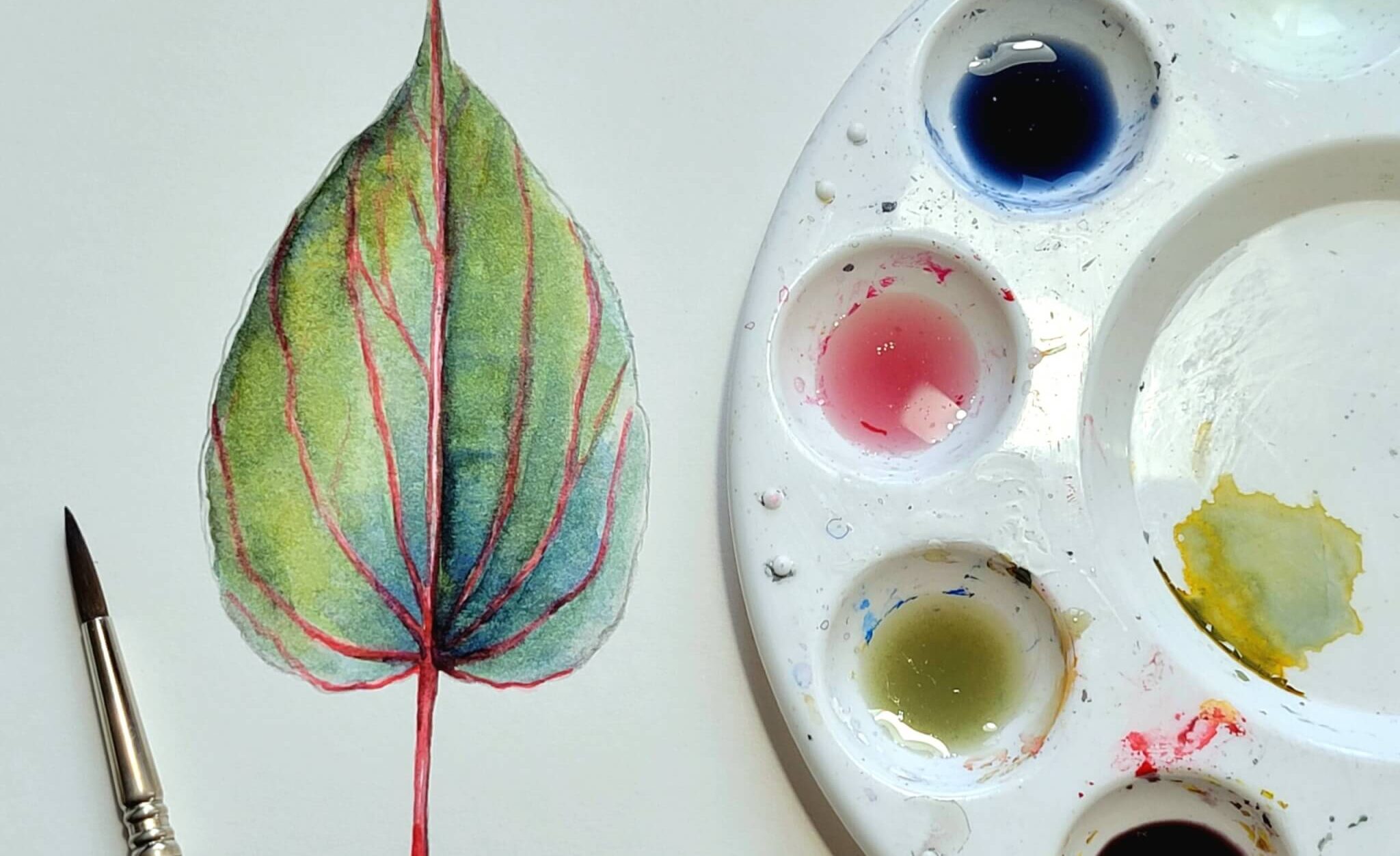 Water color palette beside water color of a leaf.