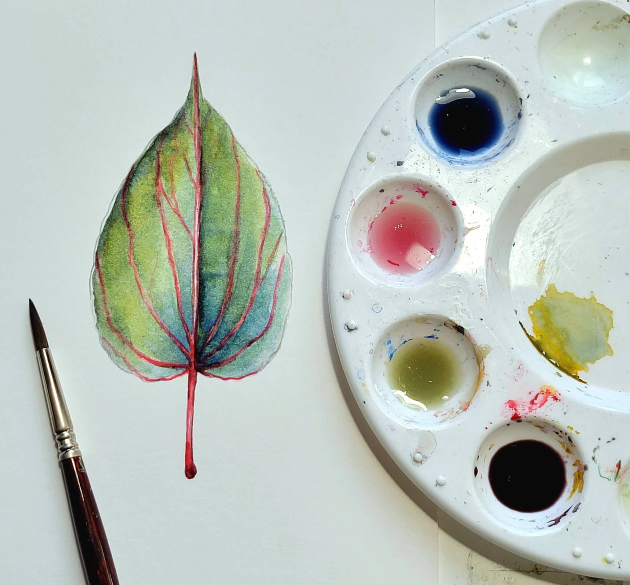 Water color palette beside water color of a leaf.