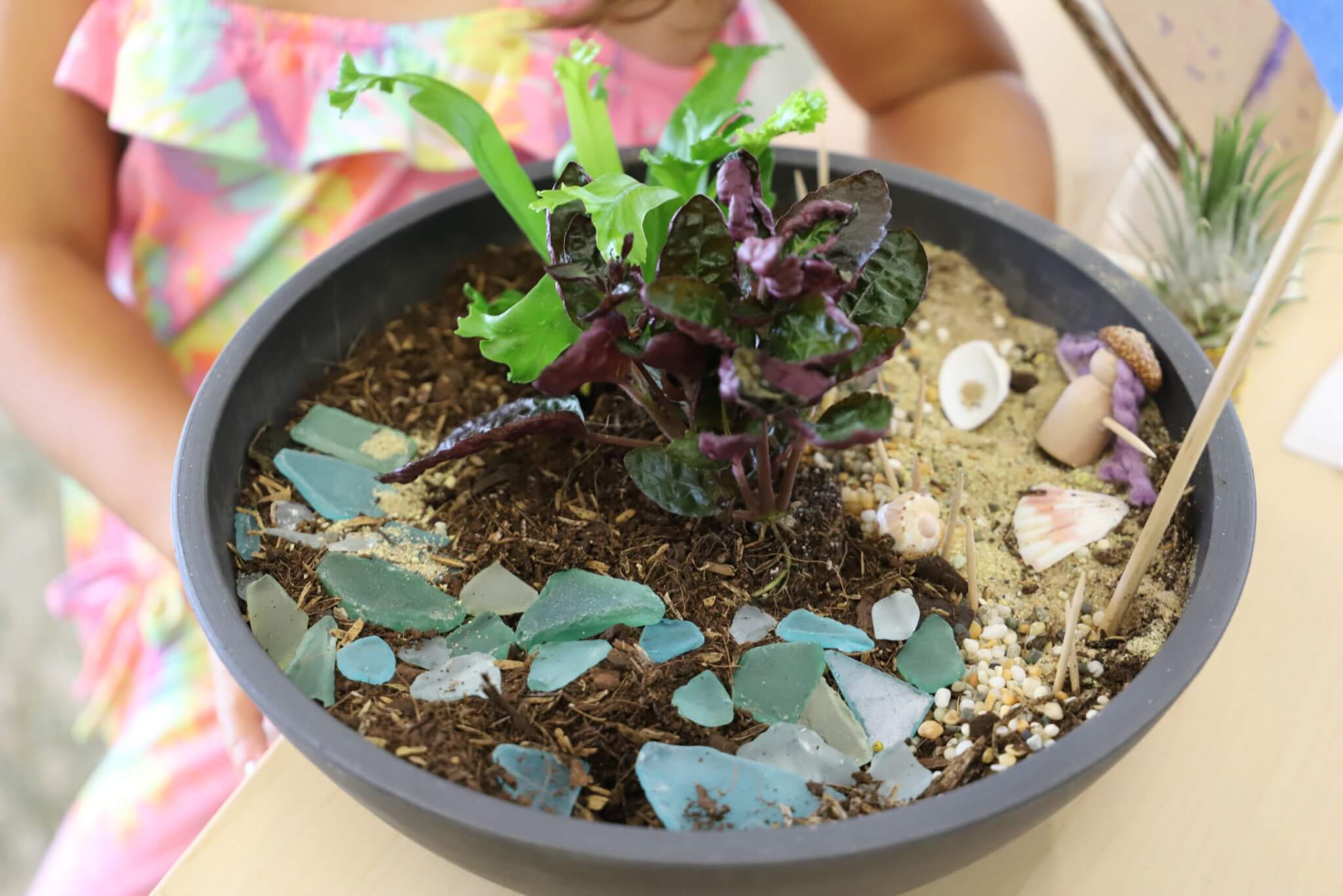 Fairy garden in a bowl with small plants and decorations.