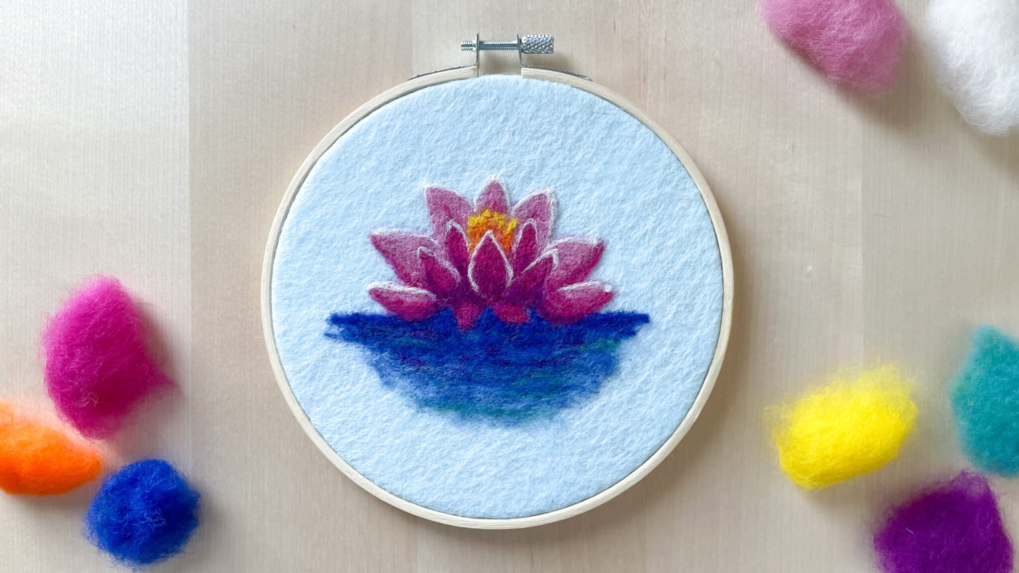 Felt design of a water lily on fabric on an embroidery hoop.