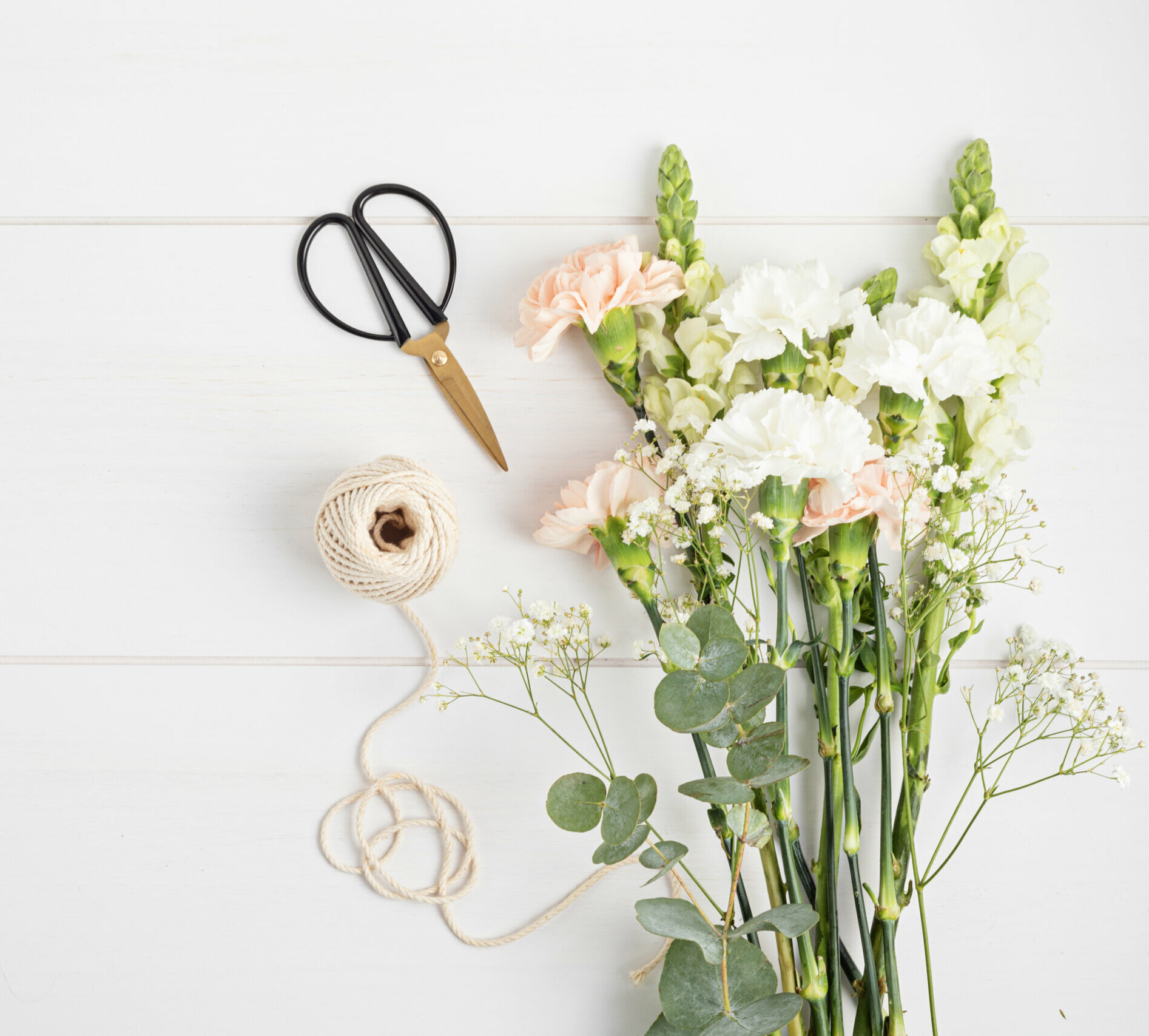 Variety of pink and white flowers next to small scissors and twine.