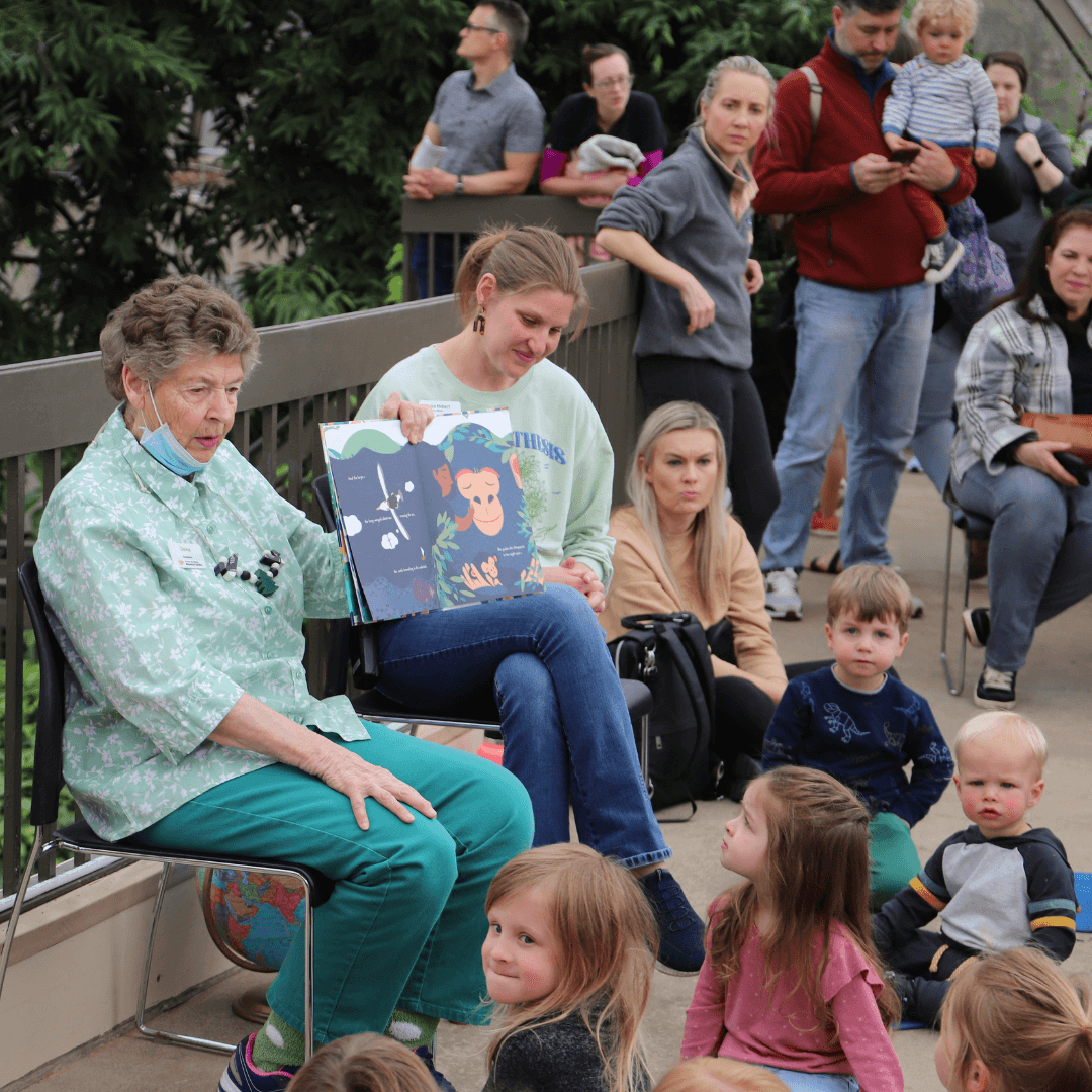 Two adults leading a story time for young children in a garden conservatory. 